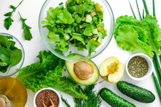 Cooking healthy diet or vegetarian food. Cutting board surrounded by green vegetables. Step by step recipe. Healthy eating. Ingredients for salad. Pattern flat lay with healthy vegetarian meal ingredients. Raw food concept. A variety of organic fruits and vegetables with avocado. Vegan menu. Fresh spinach and green onion leaves, arugula.