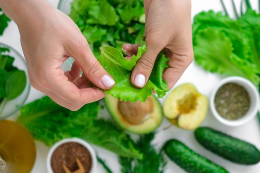 Woman cooking salad of fresh green vegetables and herbs. Cooking healthy diet or vegetarian food. Female hands cut salad surrounded by green vegetables. Step by step recipe. Healthy eating. Ingredients for salad. Pattern flat lay with healthy vegetarian meal ingredients. Raw food concept. A variety of organic fruits and vegetables with avocado. Vegan menu. Fresh spinach and green onion leaves.