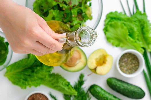 Woman cooking salad of fresh green vegetables and herbs. Cooking healthy diet or vegetarian food. Female hands add olive oil. Step by step recipe. Healthy eating. Ingredients for salad. Pattern flat lay with healthy vegetarian meal ingredients. Raw food concept. A variety of organic fruits and vegetables with avocado. Vegan menu. Fresh spinach and green onion leaves.