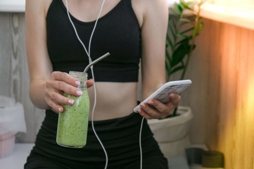 Young millenial woman checking smartphone drinking vegan smoothie drink detox. Woman doing yoga exercises at home. Online tuition Clean eating, weight loss, healthy dieting food concept. Stay healthy. Wellness