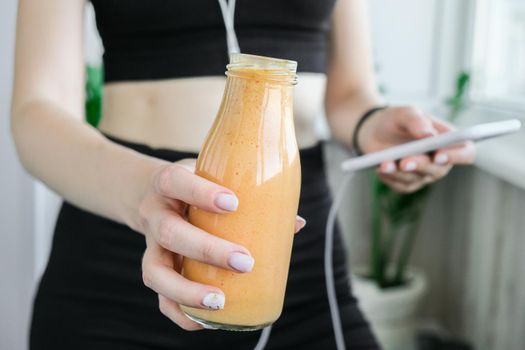 Young millenial woman checking smartphone drinking vegan smoothie drink detox. Woman doing yoga exercises at home. Online tuition Clean eating, weight loss, healthy dieting food concept. Stay healthy. Wellness