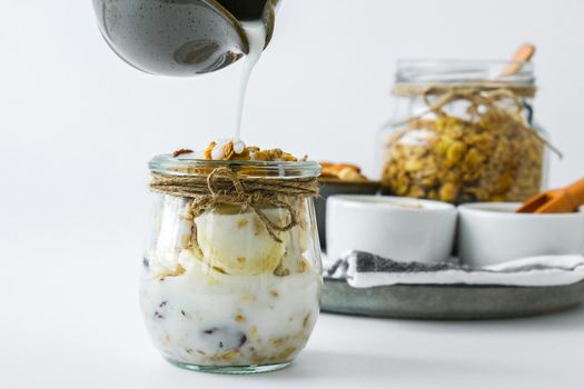 Healthy breakfast. Oatmeal Granola with greek yogurt pouring and nuts banana muesli in jars on light background. Vegan, vegetarian and weight loss diet concept. Detox menu. Healthy eating food