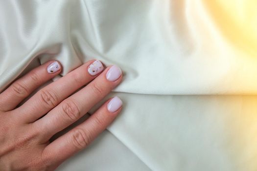 Closeup elegant pastel natural modern design manicure on fabric silk background. Female hands. Gel nails. Nude manicure. Beige color. Clean skin. Spa salon, advertisement. Skin care. Beauty. Nail care. Beauty treatment. Copy space