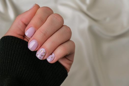 Closeup elegant pastel natural modern design manicure on fabric silk background. Female hands. Gel nails. Nude manicure. Beige color. Clean skin. Spa salon, advertisement. Skin care. Beauty. Nail care. Beauty treatment. Copy space