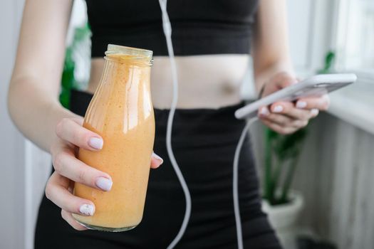 Young millenial woman checking smartphone drinking vegan smoothie drink detox. Woman doing yoga exercises at home. Online tuition Clean eating, weight loss, healthy dieting food concept. Stay healthy. Wellness