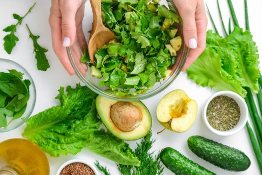 Woman mix salad of fresh green vegetables and herbs. Cooking healthy diet or vegetarian food. Step by step recipe. Healthy eating. Ingredients for salad. Pattern flat lay with healthy vegetarian meal ingredients. Raw food concept. A variety of organic fruits and vegetables with avocado. Vegan menu. Fresh spinach and green onion leaves, arugula.