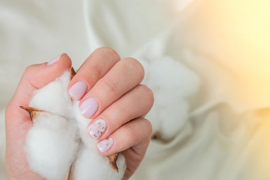 Woman hands with beautiful nude modern design manicure holding delicate white cotton flower. Female Manicure, natural look. Nails care. Self care. SPA and beauty concept