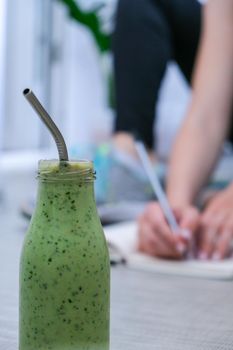 Seasonal Matcha green vegan smoothie with chia seeds and mint smoothie drink detox. Woman writing results and goals on background Clean eating, weight loss, healthy dieting food concept. Fitness training workout at home.