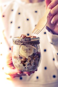 Female hands, woman eating Healthy breakfast. Oatmeal Granola with greek yogurt and nuts banana muesli in jars on light background. Vegan, vegetarian and weight loss diet concept. Detox menu. Healthy eating food