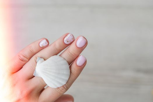 Healthy woman's hands with sea shells. Nude modern design nails. Clean skin. Soft light. Good for cosmetics. Natural colors, retouch. Long elegant fingers. Spa, medicine advertisement. Skin care. Beauty. Self care