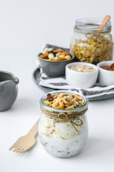 Healthy breakfast. Oatmeal Granola with greek yogurt and nuts banana muesli in jars on light background. Vegan, vegetarian and weight loss diet concept. Detox menu. Healthy eating food