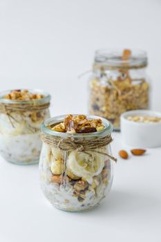 Healthy breakfast. Oatmeal Granola with greek yogurt and nuts banana muesli in jars on light background. Vegan, vegetarian and weight loss diet concept. Detox menu. Healthy eating food