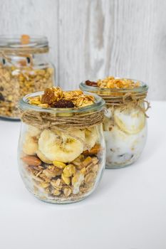 Healthy breakfast. Oatmeal Granola with greek yogurt and nuts banana muesli in jars on light background. Vegan, vegetarian and weight loss diet concept. Detox menu. Healthy eating food