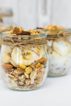 Healthy breakfast. Oatmeal Granola with greek yogurt and nuts banana muesli in jars on light background. Vegan, vegetarian and weight loss diet concept. Detox menu. Healthy eating food