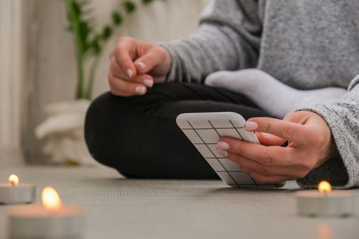 Young millennial blonde woman doing yoga exercise watching tutorial lesson on mobile phone stretching fitness at balcony home. Mindfulness meditation. The concept of online training. Video lessons. Self-isolation is beneficial. Exercise for Lose weight, increase flexibility And tighten the shape. Young slim athletic girl practices yoga at home in online lessons.