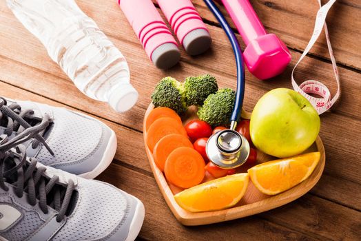 Top view of fresh fruits and vegetables in heart plate wood (apple, carrot, tomato, orange, broccoli) and sports equipment and doctor stethoscope on wooden table, Healthy lifestyle diet food concept