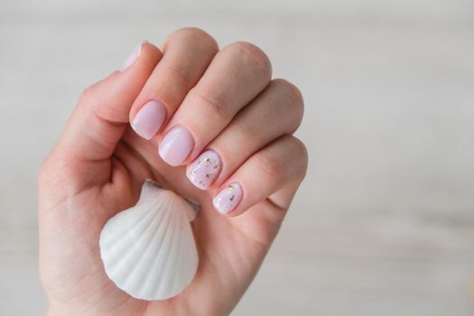 Healthy woman's hands with sea shells. Nude modern design nails. Clean skin. Soft light. Good for cosmetics. Natural colors, retouch. Long elegant fingers. Spa, medicine advertisement. Skin care. Beauty. Self care