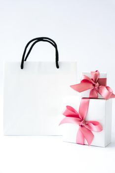 Blank paper white bag and two gift present boxes with pink ribbon on white background. Black friday sale. Shopping concept. Mockup of paper shopping bag. Copy space for text