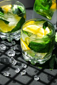 Mojito refreshing cocktail, alcohol drink. Lemonade with lemon and mint leaves on dark background. Trendy shadows Ice cubes. Summer refreshing detox drinks. Clean eating, healthy lifestyle concept, Diet. Nutrition