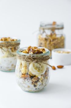 Healthy breakfast. Oatmeal Granola with greek yogurt and nuts banana muesli in jars on light background. Vegan, vegetarian and weight loss diet concept. Detox menu. Healthy eating food