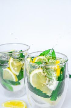 Mojito refreshing cocktail, alcohol drink. Lemonade with lemon and mint leaves on light background. Ice cube fall splash drops. Summer refreshing detox drinks. Clean eating, healthy lifestyle concept, Diet. Nutrition.