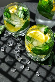 Mojito refreshing cocktail, alcohol drink. Lemonade with lemon and mint leaves on dark background. Trendy shadows Ice cubes. Summer refreshing detox drinks. Clean eating, healthy lifestyle concept, Diet. Nutrition