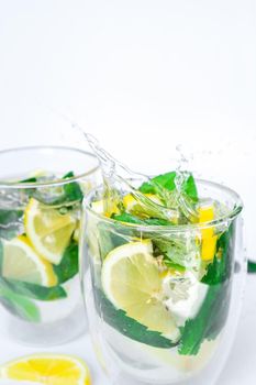 Mojito refreshing cocktail, alcohol drink. Lemonade with lemon and mint leaves on light background. Ice cube fall splash drops. Summer refreshing detox drinks. Clean eating, healthy lifestyle concept, Diet. Nutrition.