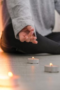 Close-up. Woman doing yoga exercise at home. Mindfulness meditation. Relax breathe easy pose gym healthy lifestyle concept. Burning candles light. Lotus asana. Atmosphere of relax and zen. Exercise to reach clarity of mind and perfect body. Padmasana