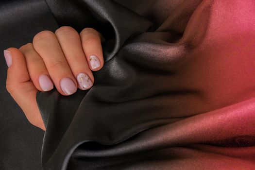 Closeup elegant pastel natural modern design manicure on fabric silk background. Female hands. Gel nails. Nude manicure. Beige color. Clean skin. Spa salon, advertisement. Skin care. Beauty. Nail care. Beauty treatment. Copy space