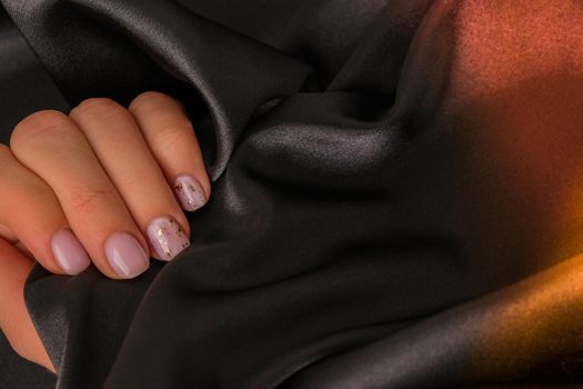 Closeup elegant pastel natural modern design manicure on fabric silk background. Female hands. Gel nails. Nude manicure. Beige color. Clean skin. Spa salon, advertisement. Skin care. Beauty. Nail care. Beauty treatment. Copy space