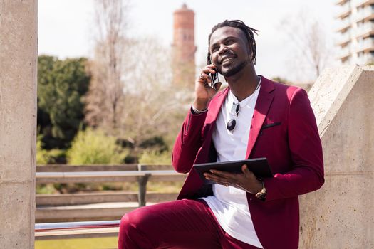 smiling black businessman using a tablet and talking on smart phone outdoors in the city, technology and remote work concept, copy space for text