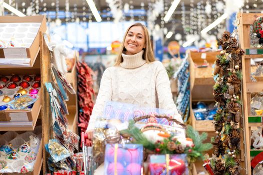 Christmas decoration shopping. Caucasian woman choose new year decor in shopping mall. Medium age female dressed white sweater buying christmas ornament toys indoor store