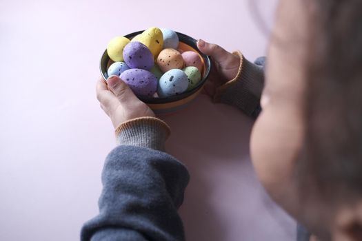 child hand holding a bowl of easter eggs on pink .