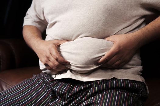 man's hand holding excessive belly fat, overweight concept.