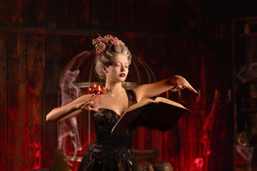 Charming woman witch flowers in hair vintage black dress with book of spell in the old castle. Halloween. Celebration. Witchcraft concept, fairy tale mystic atmosphere. Conjure magic spells
