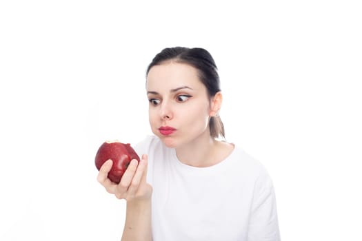 woman in white t-shirt eating red apple, white studio background. High quality photo