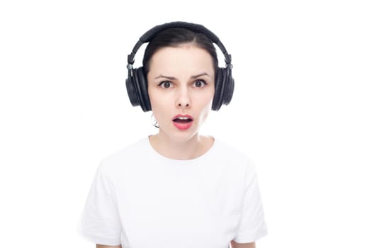 surprised brunette woman in big headphones listens to music, white background. High quality photo