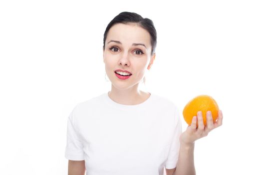 cute smiling brunette girl in a white t-shirt holding an orange in her hand, white background. High quality photo