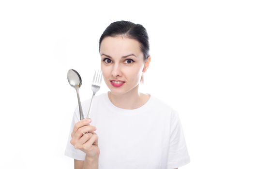 cute woman in a white t-shirt holds a spoon and fork in her hand, white studio background. High quality photo