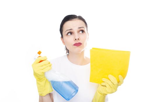 pensive woman in a white t-shirt on her hands yellow cleaning gloves holds window cleaner and rags in her hands, white background. High quality photo