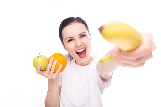 smiling woman in white t-shirt holding apple orange and banana in her hands, white background. High quality photo