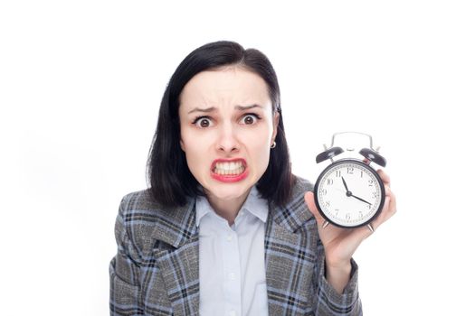 anxious female manager in office suit holding an alarm clock, white studio background. High quality photo