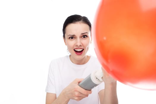 happy woman in white t-shirt inflates red balloon, white studio background. High quality photo