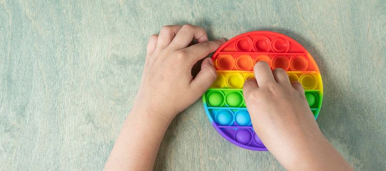 banner with Kid playing with pop it sensory toy. boy pressing on colorful rainbow squishy soft silicone bubbles. Stress and anxiety relief. Trendy fidgeting game. top view