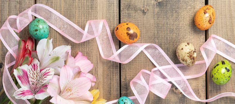 banner with multicolored alstroemeria, pink, yellow, magenta, white and red alstroemerias with painted quail eggs. background from multi-colored flowers and painted eggs with pink ribbon on wooden table.Top view