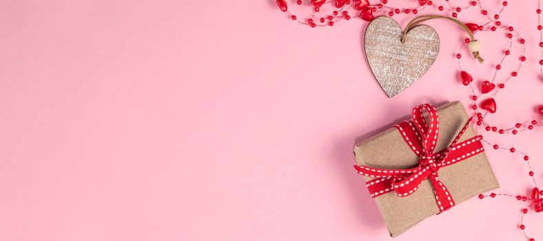 banner with One wooden heart and gift with red ribbon near beads with hearts on pastel pink colors. Valentine's Day background. Valentine's Day concept. Flat lay. Top view. Copy space