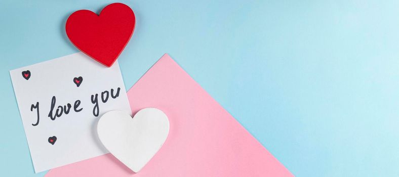 banner with Valentine's Day background. Red and white hearts and note with the words I love you on pastel blue and pink colors. Valentine's Day concept. Flat lay. Top view.