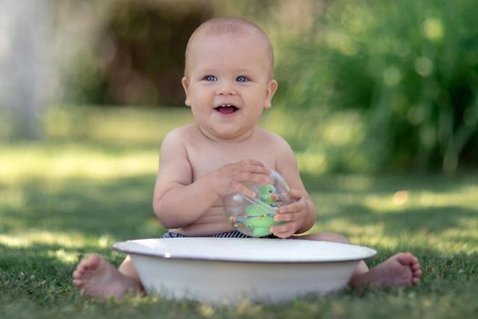 Cute baby hot summer day playing with a tub of water in the garden and smiling to the camera
