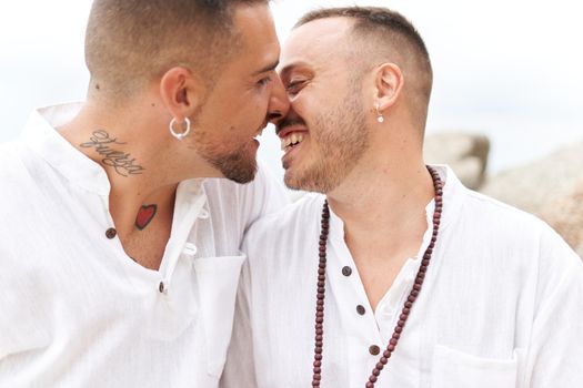 Homosexual couple smiling tenderly while kissing on a topical beach