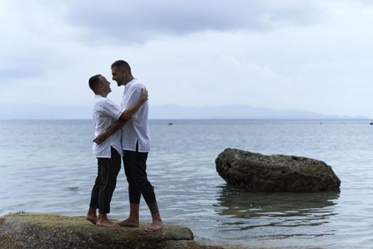 Gay couple about to kiss while embracing next to the ocean in an island of Thailand